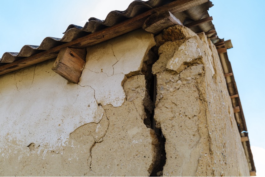 Uma vista de perto de uma parede severamente rachada e danificada com uma rachadura na parede e um telhado de metal corrugado.