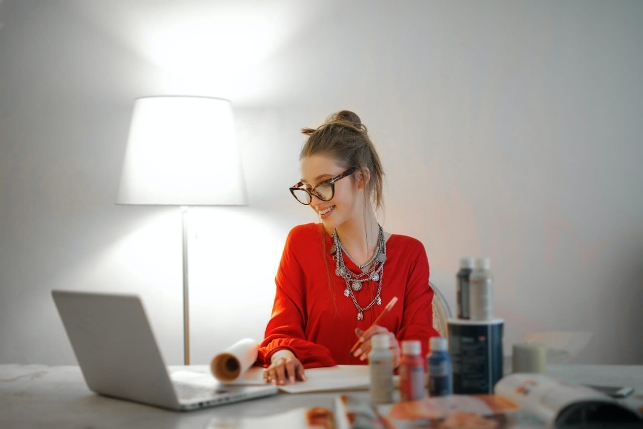 Uma mulher sentada em uma mesa com um laptop em frente a uma luminária.