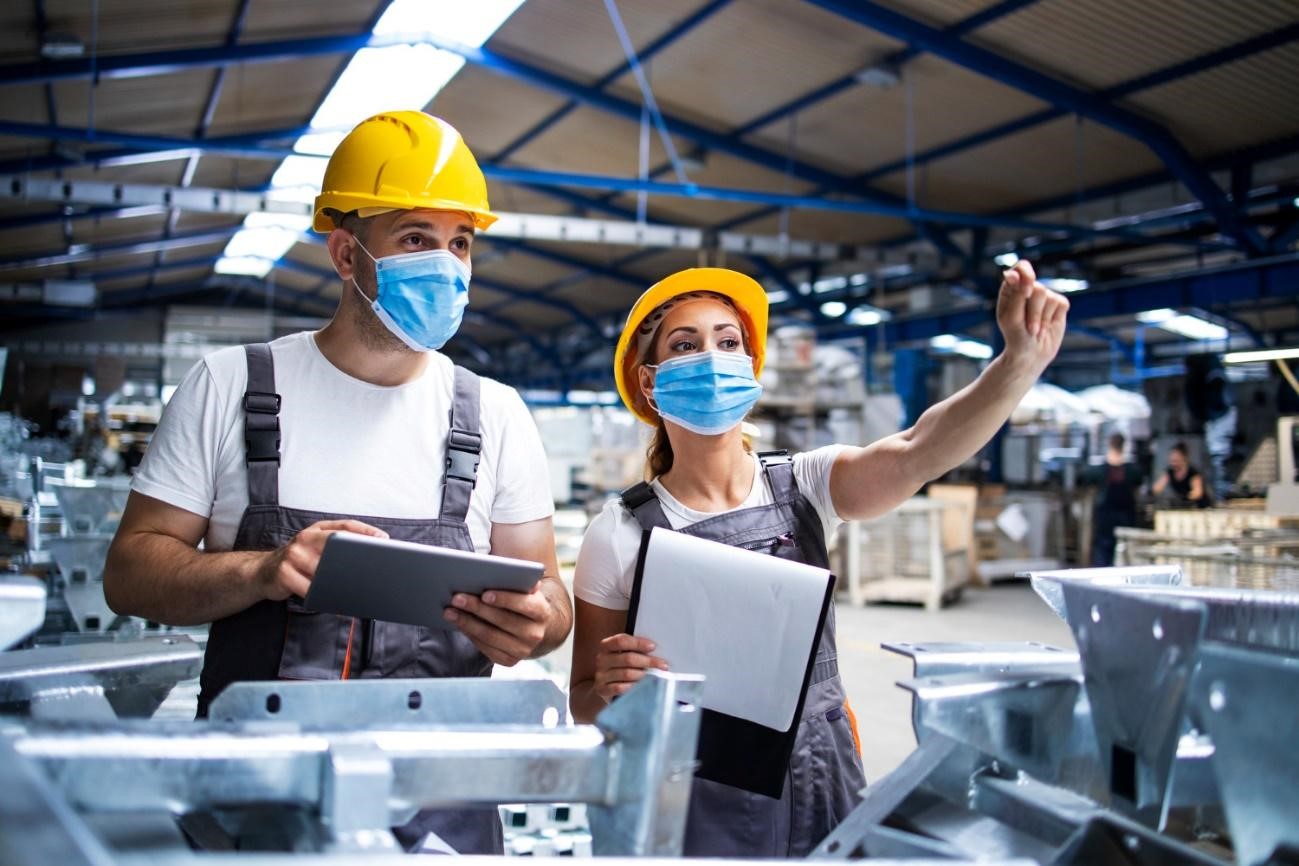 Dois trabalhadores praticando manufatura enxuta, usando máscaras protetoras em uma fábrica.