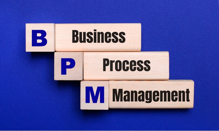 Blocos de madeira dispostos em degraus exibindo as palavras "Business Process Management" com as iniciais BPM na lateral, sobre um fundo azul.