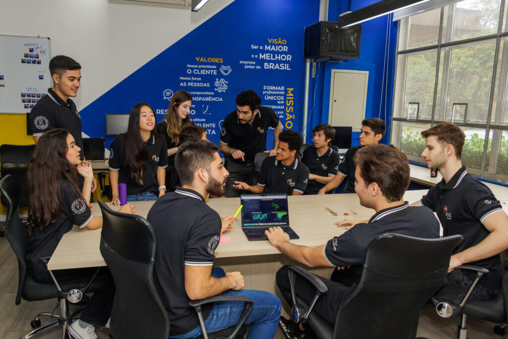 time da poli junior fazendo consultoria em gestão empresarial, reunidos em uma sala cm uma mesa de reunião ao centro