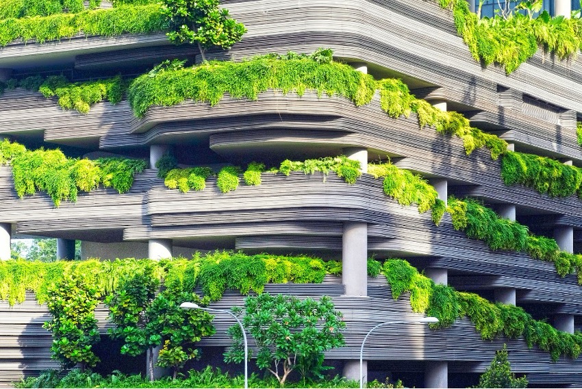 Edifício de vários andares em betão, com inúmeras varandas decoradas com extensos verdes e vinhas, apresentando uma mistura de arquitectura e natureza, exemplificando a construção sustentável.