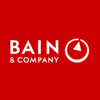 Logotipo da Bain & Company, com o nome da empresa em texto branco e um ícone circular abstrato que lembra uma bússola em um fundo vermelho, simbolizando sua abordagem integrativa aos workshops.