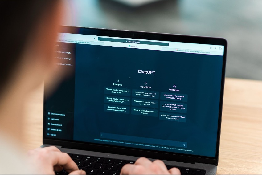 Pessoa que usa um laptop exibindo a interface ChatGPT, que inclui seções com exemplos, recursos e limitações em uma tela com tema escuro. Esta IA poderosa mostra como a inteligência artificial pode ser utilizada em várias aplicações para melhorar a experiência do usuário.
