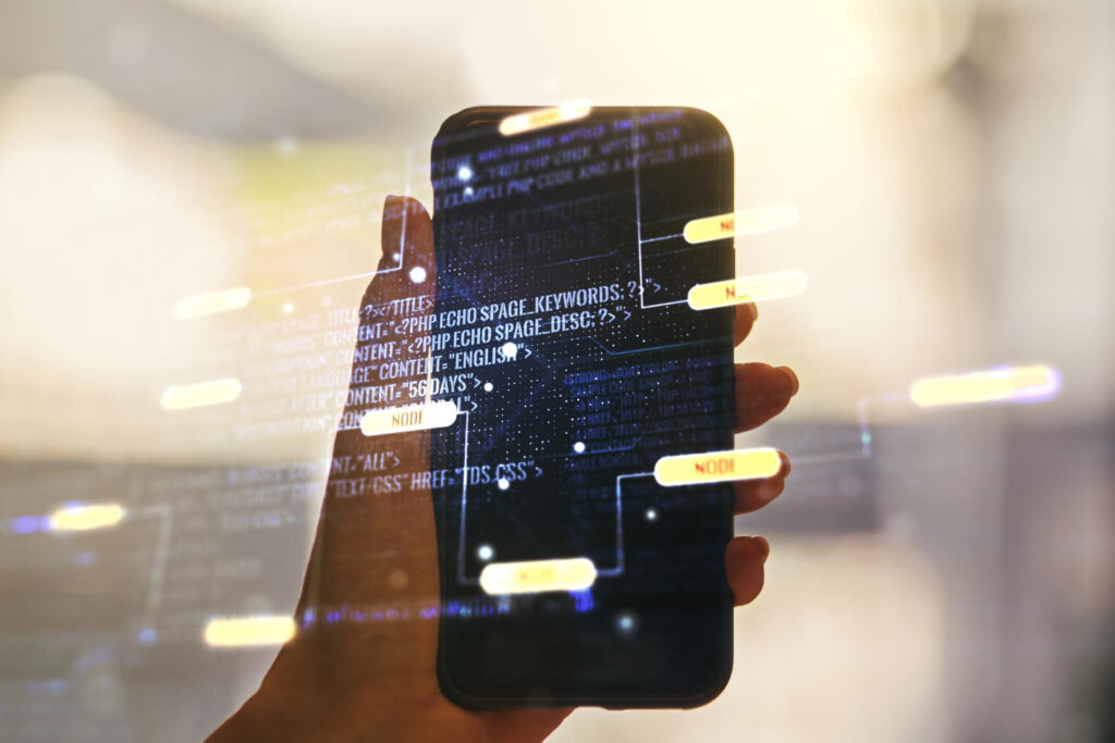 Mão segurando smartphone com códigos de programação projetados, representando conceitos tecnológicos e desenvolvimento de aplicativos.