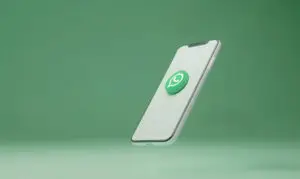 Smartphone moderno branco com o ícone flutuante do WhatsApp em 3D, sobre fundo verde-claro. Conceito de comunicação digital.