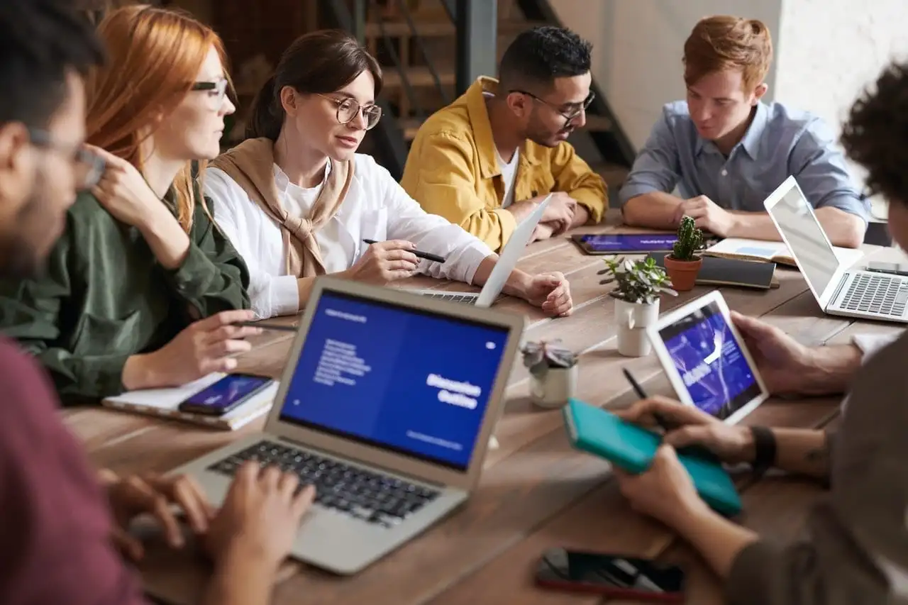 Um grupo de pessoas sentadas ao redor de uma mesa com laptops.