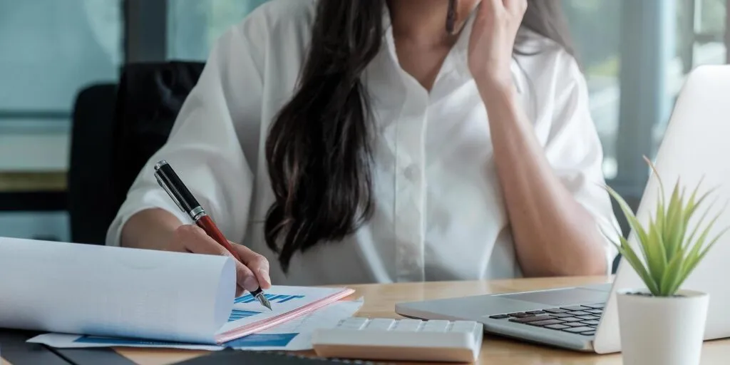 Uma mulher sentada em uma mesa com um laptop e papéis, trabalhando em consultoria para empresas.