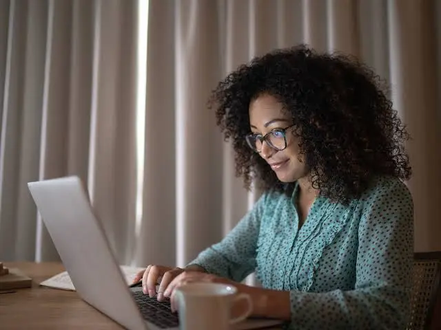 Uma mulher realizou consultoria para empresas em seu laptop em frente a uma janela.