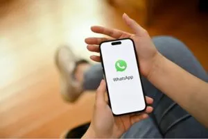 Uma pessoa segura um smartphone exibindo o logotipo do WhatsApp na tela, destacando suas utilidades para vários tipos de comunicação, incluindo chatbots.